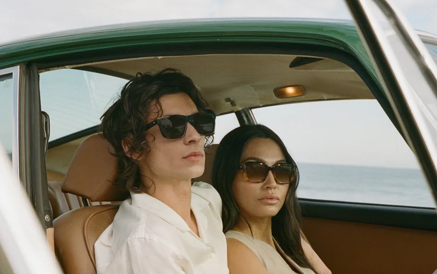 Homme et femme en lunettes de soleil Barton Perreira à bord d'une voiture ancienne au bord de la mer